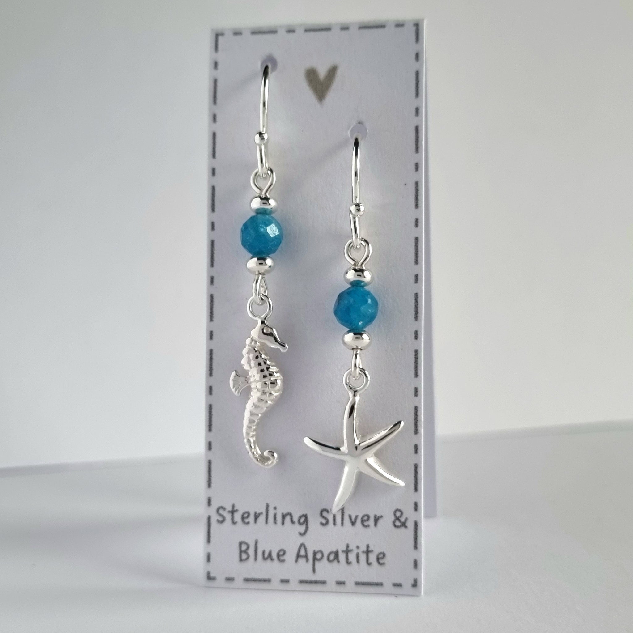 Ocean themed silver earrings with blue Apatite gemstones. One earring features a silver starfish and the other earring features a silver starfish.