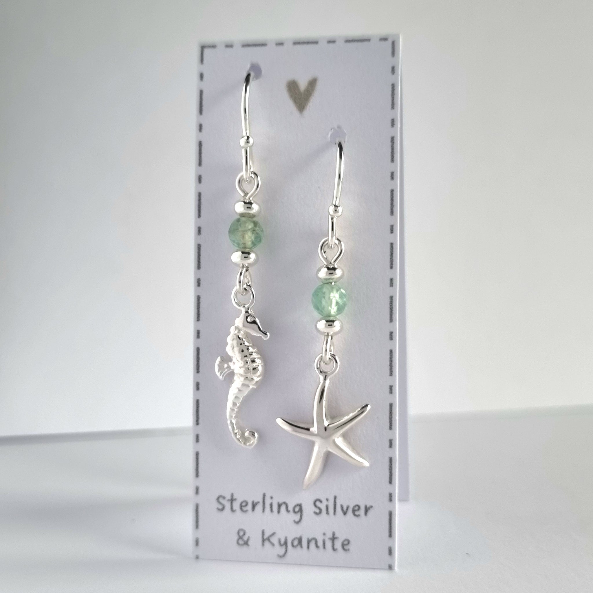 Ocean themed silver earrings with a silver starfish on one earring and silver seahorse on the other earring. Both earrings feature a sparkly pale green kyanite gemstone bead