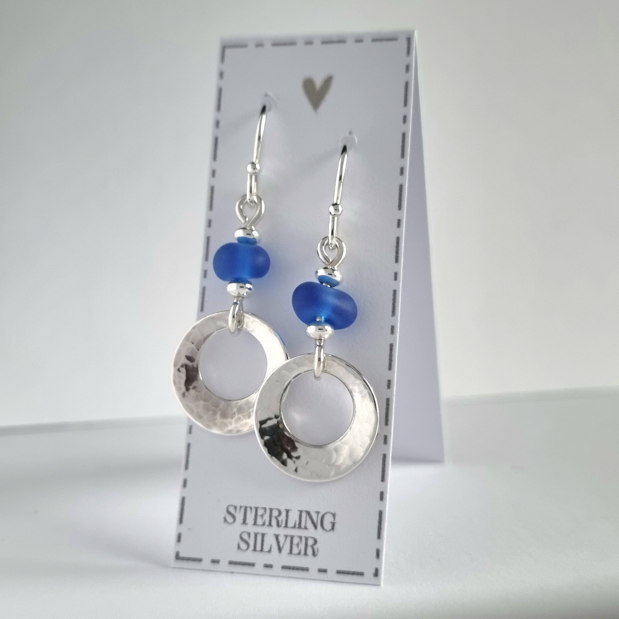Beautiful, hammered silver earrings, featuring genuine sea glass beads in a deep cobalt blue colour. These sterling silver offset circles feature a gentle hammered texture and a softly concave finish.