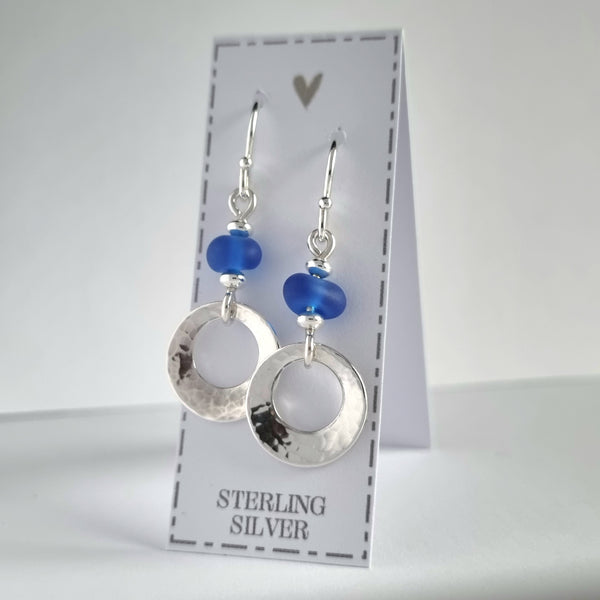 Beautiful, hammered silver earrings, featuring genuine sea glass beads in a deep cobalt blue colour. These sterling silver offset circles feature a gentle hammered texture and a softly concave finish.