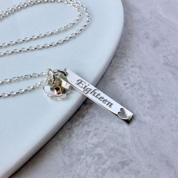 18th birthday necklace, a sterling silver bar pendant engraved with eighteen on the front and the birthday girls name on the back. A silver flower charm is also added to the chain and sits beside the bar.