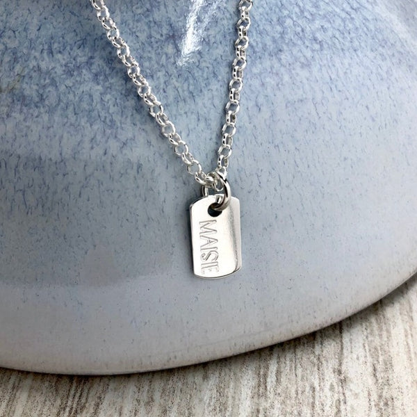 tiny dog tag necklace engraved in sterling silver with any name or word up to 6 letters. All letters engraved in capitals. Tag measures 7mm wide and 13mm high.